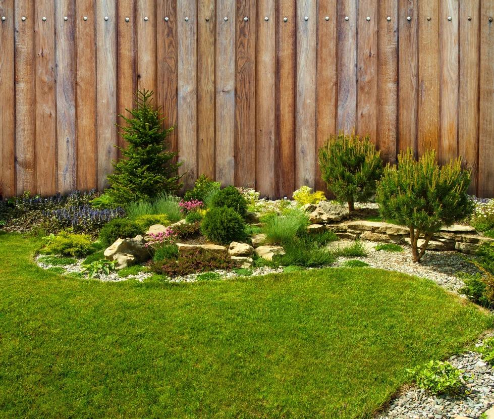 Jardin paysager avec pelouse entretenue, massifs floraux colorés délimités par bordures buis taillées, topiaires coniques, allées gravillonnées
