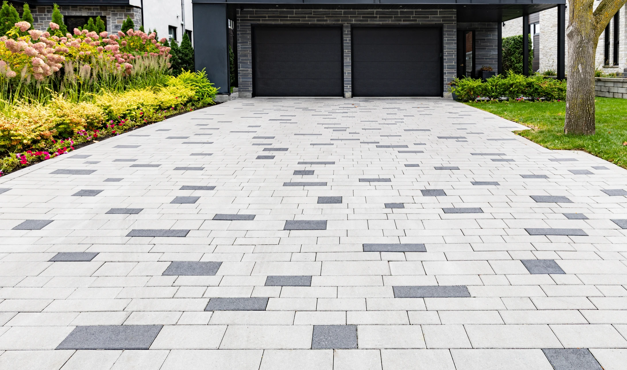 Ouvrier en équipement de sécurité orange et casque blanc installant du pavage extérieur, agenouillé sur dalle béton, utilisant outil de coupe sur pavés gris