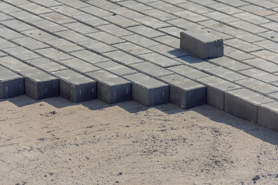 Ouvrier en chantier extérieur installant des pavés en béton sur lit de sable, utilisant un maillet à manche jaune pour ajuster l'alignement